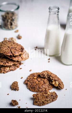 Flaschen Milch mit Schokoladen-Cookies und Glas Walnüsse auf Tisch, Nahaufnahme Stockfoto