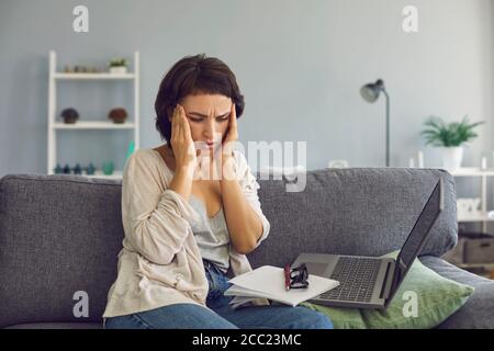 Überarbeiteter Freiberufler mit Kopfschmerzen in der Nähe von Laptop zu Hause. Gestresste Frau mit professionellem Burnout drinnen Stockfoto