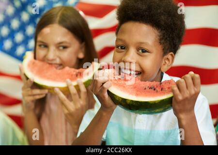Porträt eines lächelnden afrikanischen Jungen hält Wassermelone und Blick auf die Kamera mit amerikanischer Flagge im Hintergrund, kopieren Raum Stockfoto