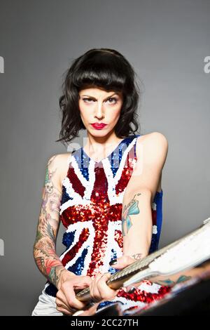 Junge Frau mit Gitarre und Tattoo auf der Hand vor grauem Hintergrund, Porträt Stockfoto