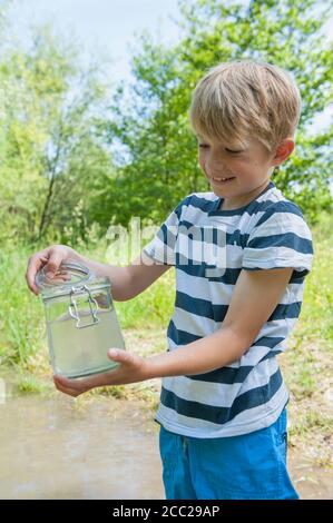 Deutschland, Bayern, München, junge Füllwasser in Glas am See, Lächeln Stockfoto