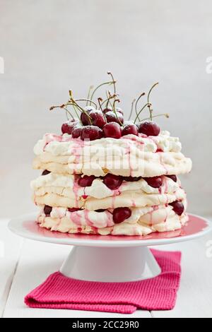 Pavlova mit Schlagsahne, Kirschen, Kirschsauce und Puderzucker auf Kuchenplatte, Nahaufnahme Stockfoto