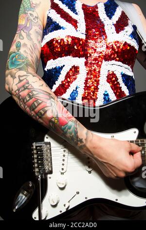 Nahaufnahme einer jungen Frau, die Gitarre und Tattoo spielt Ihre Hand vor grauem Hintergrund Stockfoto