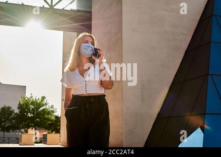 Junge Frau spricht am Telefon, während sie eine Maske trägt Stockfoto