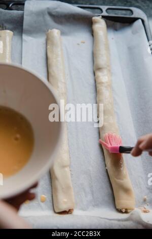 Draufsicht der Person, die rohes Ei auf Brötchen schmiert, während Gebäck wird vorbereitet Stockfoto