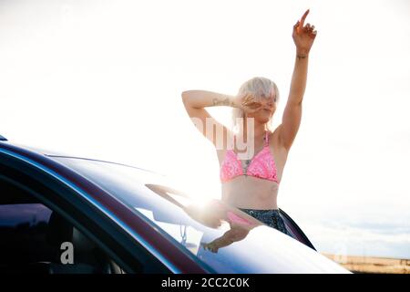 Junge Frau, die in einem Bikini vor ihrem Auto tanzt Die Sonne Stockfoto