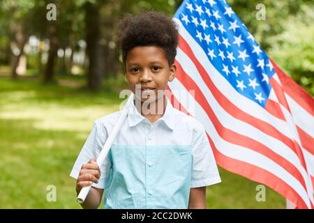 Waist up Porträt von lächelnden afrikanischen Jungen mit amerikanischer Flagge, während im Freien im Park stehen, kopieren Raum Stockfoto