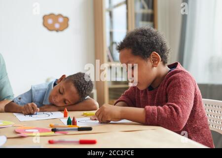 Seitenansicht Porträt von afroamerikanischen Jungen Zeichnung Bilder mit Buntstiften, während genießen Art-Klasse in der Vorschule, kopieren Raum Stockfoto