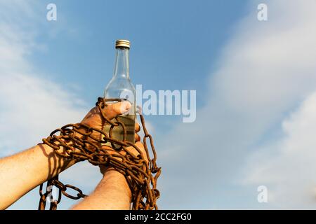 Hand an eine Flasche Alkohol gekettet, gegen den blauen Himmel Stockfoto