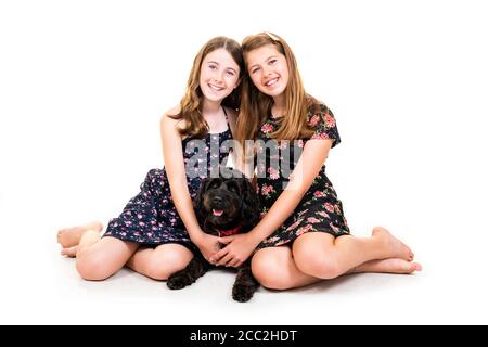Horizontales Porträt von zwei jungen Schwestern mit ihrem Haustier Hund auf weißem Hintergrund in einem Studio oder High-Key. Stockfoto