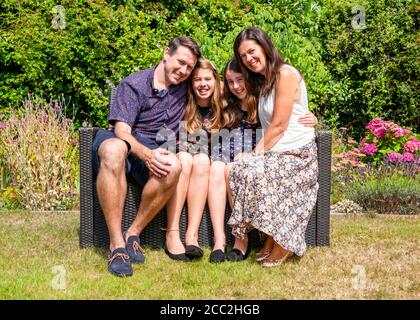 Horizontales Porträt einer jungen Familie, die in ihrem Garten eng beisammen sitzt. Stockfoto