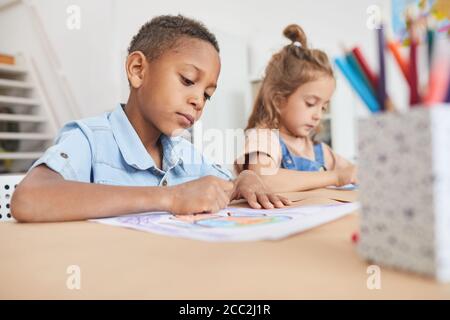 Portrait von niedlichen afroamerikanischen Jungen Färbung Bilder mit Buntstiften, während genießen Kunst und Handwerk Klasse in der Vorschule oder Kinder Entwicklungszentrum, Stockfoto