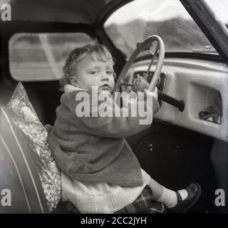 1960er Jahre, historisches, junges Mädchen, das auf einem Fahrersitz eines Autos der Epoche sitzt, das das Lenkrad hält, England, Großbritannien. Stockfoto