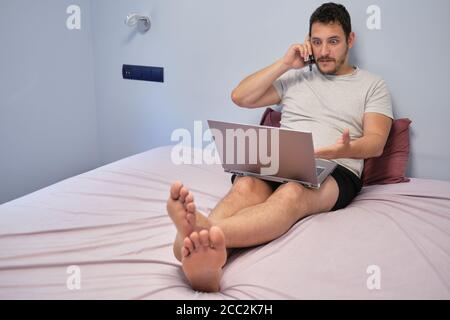 Junger Erwachsener, der mit jemandem über etwas spricht, das er auf dem Laptop beobachtet. Er ist überrascht. Arbeiten von zu Hause Konzept. Stockfoto