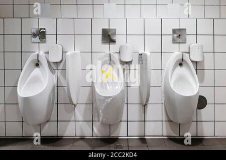 Verbotsband und Distanzaufkleber Schild mit Plastikfolie über Das Urinal in einer öffentlichen Toilette für die Menschen zu Folgen Sie der sozialen Distanzierung, um in zu vermeiden Stockfoto