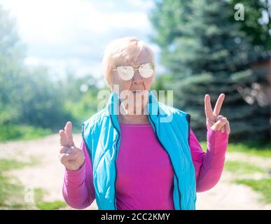Fröhliche, modische 90-jährige Großmutter mit grauen Haaren, Sonnenbrille und einem Lächeln in der Natur an einem sonnigen Sommertag. Stockfoto