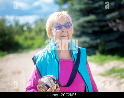 Fröhliche, modische 90-jährige Großmutter mit grauen Haaren, Sonnenbrille und einem Lächeln in der Natur an einem sonnigen Sommertag. Stockfoto