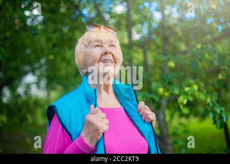 Fröhliche, modische 90-jährige Großmutter mit grauen Haaren, Sonnenbrille und einem Lächeln in der Natur an einem sonnigen Sommertag. Stockfoto