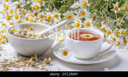 Ländliche Stillleben - Tasse gebrühten Kamillentee auf dem Hintergrund eines Straußes von Gänseblümchen, Nahaufnahme Stockfoto