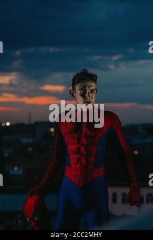Cosplayer im Bild eines Charakters Spider-man steht auf dem Dach des Hauses vor dem Hintergrund des Sonnenuntergangs Himmel und Stadt. Stockfoto