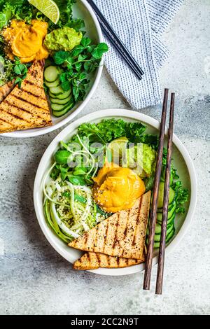 Buddha-Schüssel mit Zucchini-Pasta, gegrilltem Tofu, Guacamole, Süßkartoffel-Hummus und Gemüse, grauer Hintergrund. Stockfoto