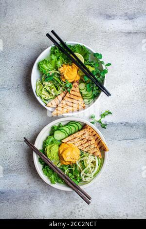 Buddha-Schüssel mit Zucchini-Pasta, gegrilltem Tofu, Guacamole, Süßkartoffel-Hummus und Gemüse, grauer Hintergrund. Stockfoto