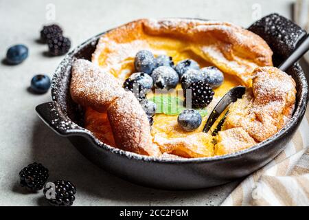 Holländischer Baby-Pfannkuchen mit Beeren und Puderzucker in einer Pfanne. Stockfoto