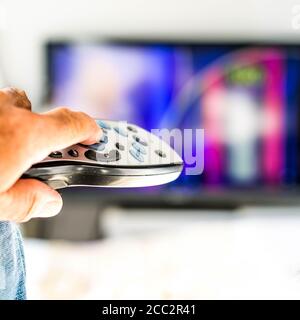 Annonymer Mann hält EINE TV-Fernbedienung, zeigt auf EIN Fernsehgerät Stockfoto