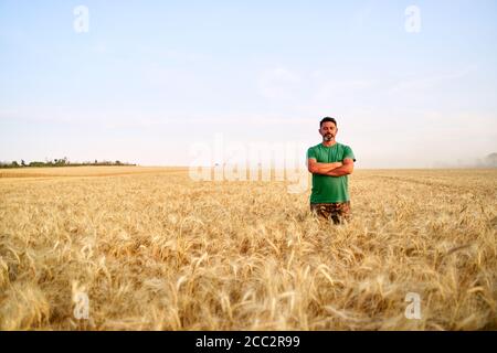 Glücklicher Bauer stolz im Weizenfeld mit gekreuzten Armen auf der Brust. Agronom trägt Corporate Uniform, Blick auf die Kamera auf Ackerland. Reich Stockfoto