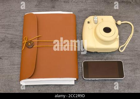 Gelbe Kamera, ein Leder-Notebook und Smartphone auf einem schwarzen Tisch. Draufsicht Stockfoto