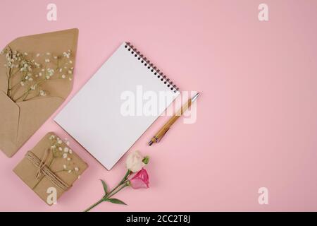 Schöne Ferienwohnung Lay Komposition mit Holzfeder, Copybook, Geschenk oder Geschenke Schachteln und Kraftpapier Umschlag auf pastellrosa Hintergrund mit Stockfoto