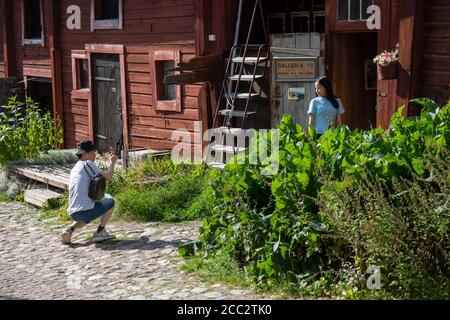 Touristen, die Reisebilder gegen das hölzerne rot-ockerfarbene Lagergebäude in der Altstadt von Porvoo, Finnland, machen Stockfoto