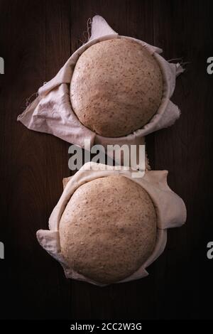 Hausgemachter, ungekochter Teig, roh im Gärkorb auf rustikalem Holztisch, fertig zum Backen, gemeines Mehl mit Vollkornbrot Stockfoto