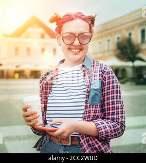 Schöne moderne junge weibliche Teenager Porträt mit außergewöhnlicher Frisur in kariertem Hemd mit "Coffee to go" Kappe und schlankes Smartphone. Modern te