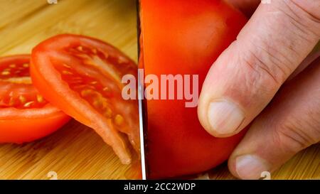 Die Hände des Küchenchefs schneiden saftige reife Tomaten mit Küchenmesser auf Holzschneidebrett. Nahaufnahme. 16x9-Format. In Innenräumen. Stockfoto