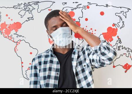 Porträt des jungen afrikanischen Kerl mit hohem Fieber und Kopfschmerzen während Coronavirus Pandemie. Krank schwarzen Mann berühren Stirn, in medizinische Maske. Weltkarte Stockfoto