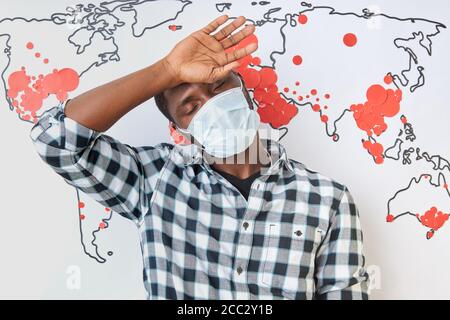 Junger afrikanischer Mann mit hohem Fieber während der Coronavirus-Pandemie auf der ganzen Welt. Mann in medizinischer Maske stehen im Hintergrund der Weltkarte. Stockfoto