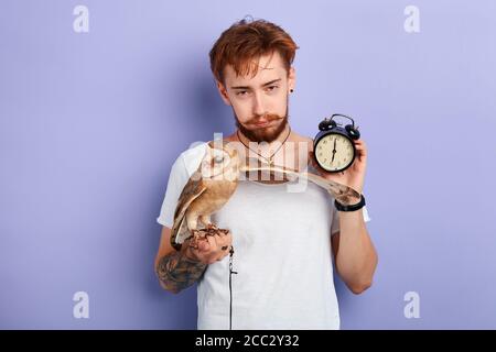 Betrunkener Typ zeigt die Uhr, sein Vogel hat ihn am frühen Morgen geweckt, isolierter blauer Hintergrund, Frustration, Depression Stockfoto