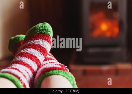 Füße Beine im Winter Kleidung Wolle Socken am Kamin Hintergrund. Frau sitzt zu Hause auf Winter oder Herbst am Abend entspannen und aufwärmen. Winter und Kälte Konzept. Hygge Heiligabend Stockfoto