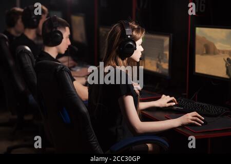 Rückseite einer jungen Frau, die ein Headset auf ihrem langen trägt Blonde Haare nimmt an Online-Cyber-Spiele-Turnier in Internetcafé Stockfoto