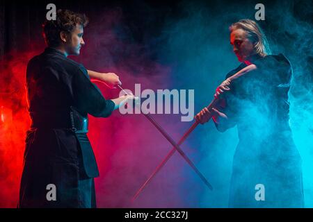 Zwei kaukasische Kendo Kampfkunstkämpfer kämpfen Kampf in Silhouette isoliert bunten rauchigen Raum, Neonlichter. Kampf, Kendo Konzept Stockfoto