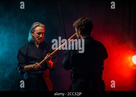 Zwei kaukasische Kendo Kampfkunstkämpfer kämpfen Kampf in Silhouette isoliert bunten rauchigen Raum, Neonlichter. Kampf, Kendo Konzept Stockfoto