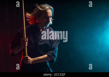 Selbstbewusster, starker, reifer Kendo-Krieger mit Shinai in den Händen, Vorbereitung auf Kendo-Wettkämpfe, Kampf. Isolierter, rauchiger Raum Stockfoto
