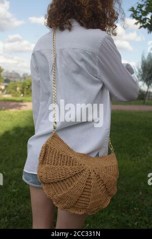 Junges Mädchen in weißem Hemd mit lockigen Haaren trägt ein Stricktasche Stockfoto