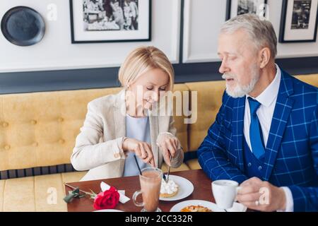 Schöne blonde stilvolle Geschäftsfrau Schneiden der Kuchen beim Abendessen mit Ehemann. Close up photo.couple mit einem Snack im Café Stockfoto