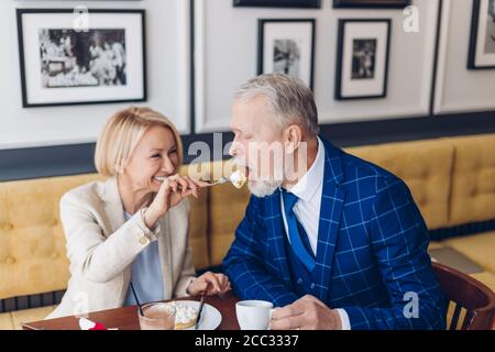 Ältere glückliche Familie Paar essen Kuchen im Café zusammen. Nahaufnahme Foto. Positive schöne Frau Behandlung ihres Mannes mit leckeren Dessert Stockfoto