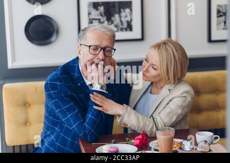 Ehrfürchtige blonde Frau beruhigt sich ihren ernsten Ehemann, während eine Pause im Café. Stockfoto