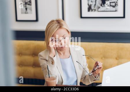 Reife Frau Auffrischung ihr Make-up am Arbeitsplatz. Nahaufnahme Foto. Attraktive Frau mit einigen Problemen mit ihren Augen Stockfoto