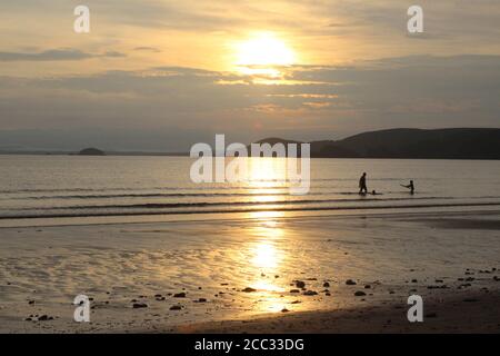 Menschen, die bei Sonnenuntergang im Meer spielen, Newgale, Pembrokeshire, Wales, Großbritannien, August 2020 Stockfoto