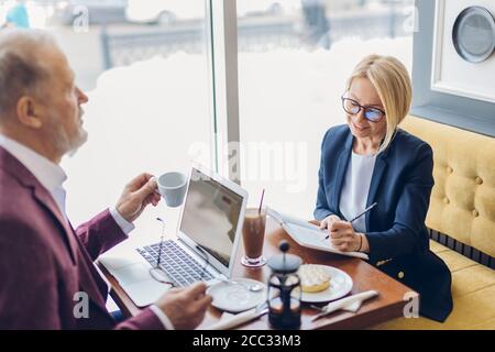 Charmante blonde Frau und alten Mann mit Frühstück und diskutieren einen Businessplan. Nahaufnahme Foto. Freizeitkonzept Stockfoto